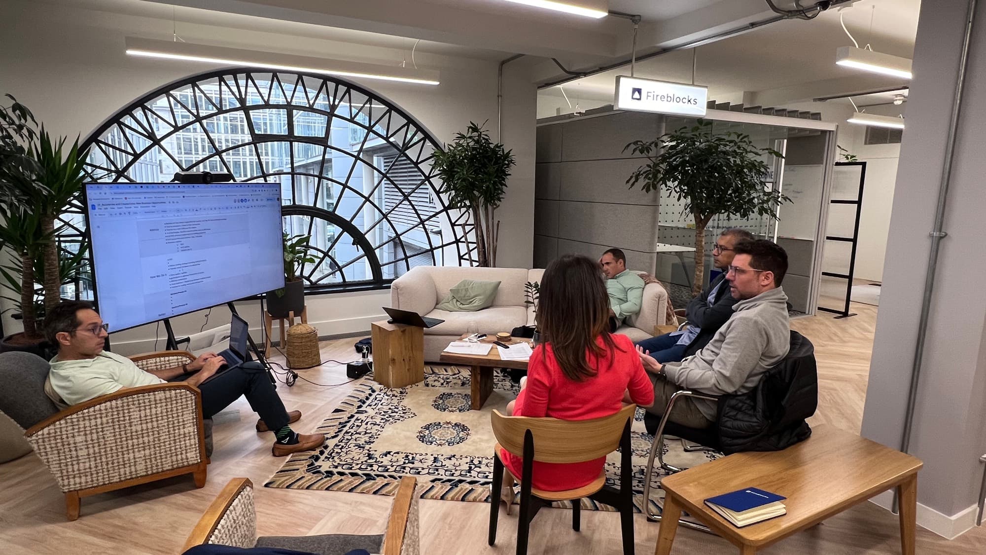 Six people in an informal office space, laptops out, looking at a document on a screen.