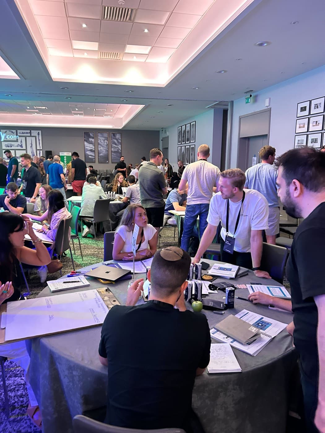 A room of tables mid exercise, people standing and talking in groups.